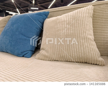 A stylish beige sofa with beige and blue throw pillows, available for sale in a furniture store A stylish beige sofa with beige and blue throw pillows, available for sale in a furniture store 141165886