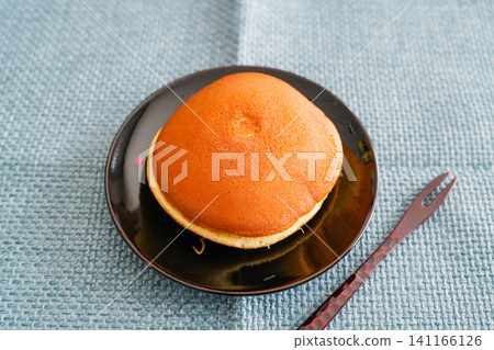 A dorayaki (Japanese sweet pancake) placed on a black plate and photographed against a blue matte background. A dorayaki (Japanese sweet pancake) placed on a black plate and photographed against a blue matte background. 141166126