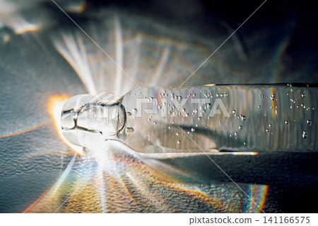 Pipette drawing cosmetic serum with vibrant light refraction 141166575