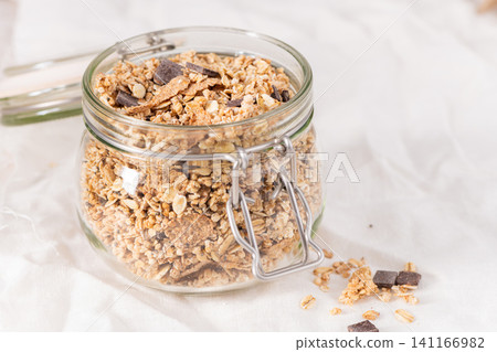Crunchy granola with chocolate chunks in a glass jar set on a clean white fabric background for a wholesome breakfast or healthy morning snack Crunchy granola with chocolate chunks in a glass jar set on a clean white fabric background for a wholesome breakfast or healthy morning snack 141166982
