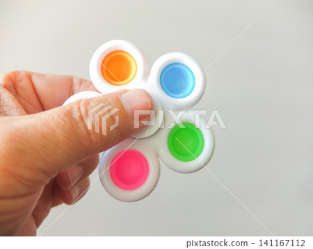 Hand holding a white flower shaped pop it fidget spinner toy on white background. Hand holding a white flower shaped pop it fidget spinner toy on white background. 141167112