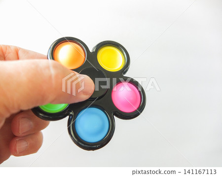 Hand holding a black flower shaped pop it fidget spinner toy on white background. Hand holding a black flower shaped pop it fidget spinner toy on white background. 141167113