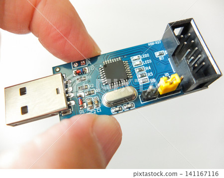 Hand holding a blue electronic PCB board with USB interface and IDC connector. 141167116
