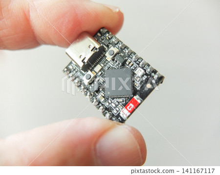 Hand holding a small black microchip microcontroller development board with type-c Hand holding a small black microchip microcontroller development board with type-c 141167117