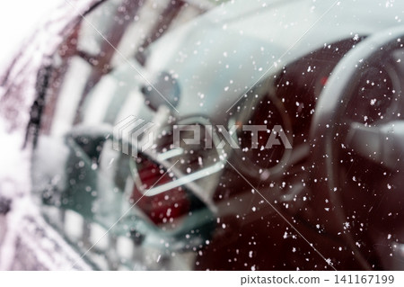 Close-up of a car windshield covered with delicate snowflakes. Through the glass, the steering wheel and dashboard are visible, creating a layered composition of crystalline patterns and interior Close-up of a car windshield covered with delicate snowflakes. Through the glass, the steering wheel and dashboard are visible, creating a layered composition of crystalline patterns and interior 141167199