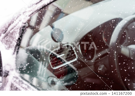 Close-up of a car window covered with delicate snowflakes. The crystalline patterns stand out against the reflective surface, where faint outlines of the surroundings appear blurred. Close-up of a car window covered with delicate snowflakes. The crystalline patterns stand out against the reflective surface, where faint outlines of the surroundings appear blurred. 141167200