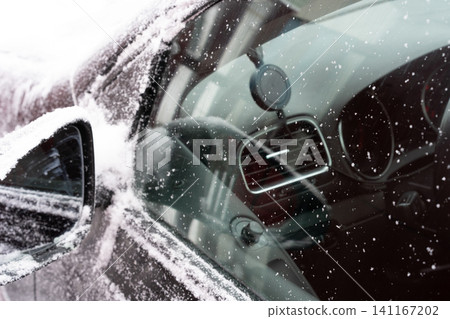 Close-up of a car driver-side window and mirror covered with snow and frost. Close-up of a car driver-side window and mirror covered with snow and frost. 141167202