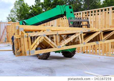 Construction workers use telehandler to lift wooden trusses at building site Construction workers use telehandler to lift wooden trusses at building site 141167259
