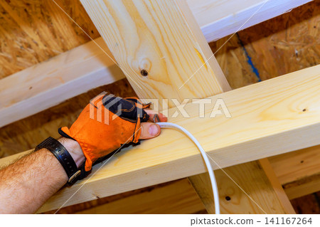 Worker installs electrical wire in wooden beams at construction site Worker installs electrical wire in wooden beams at construction site 141167264