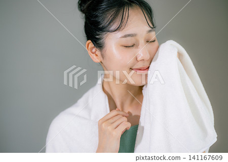 A woman washing her face and wiping it with a towel A woman washing her face and wiping it with a towel 141167609