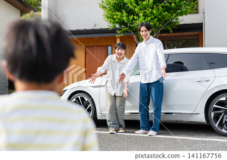 一對夫婦在自家門前和車前迎接他們的孩子。 一對夫婦在自家門前和車前迎接他們的孩子。 141167756