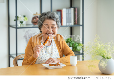 Senior woman eating mitarashi dango at home Senior woman eating mitarashi dango at home 141169449