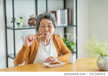 Senior woman eating mitarashi dango at home Senior woman eating mitarashi dango at home 141169451