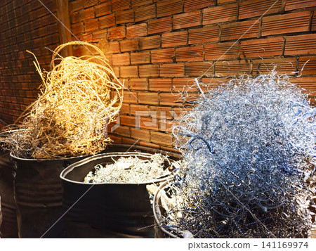Metal shavings, turnings, and swarf overflowing from barrels in a workshop against a brick wall background Metal shavings, turnings, and swarf overflowing from barrels in a workshop against a brick wall background 141169974