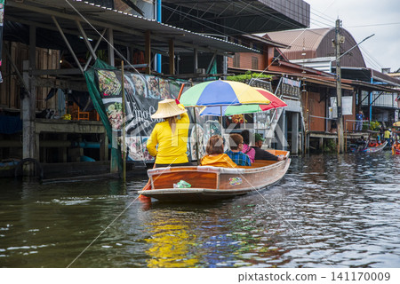 Tourists on a traditional wooden boat exploring a famous floating market in Thailand. Tourists on a traditional wooden boat exploring a famous floating market in Thailand. 141170009