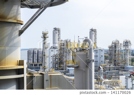 Industrial background of a large-scale chemical factory and oil refinery with complex pipelines, distillation towers, and storage tanks under a clear sky. Industrial background of a large-scale chemical factory and oil refinery with complex pipelines, distillation towers, and storage tanks under a clear sky. 141170026