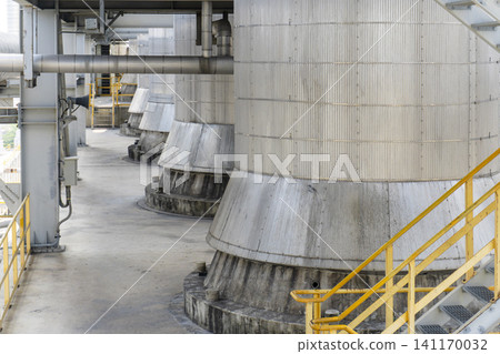 Close-up of large metal storage tanks and pipelines lined up in an industrial plant, featuring walkways with yellow safety railings. Close-up of large metal storage tanks and pipelines lined up in an industrial plant, featuring walkways with yellow safety railings. 141170032