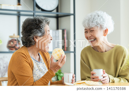 Senior woman eating rice crackers with a friend Senior woman eating rice crackers with a friend 141170386