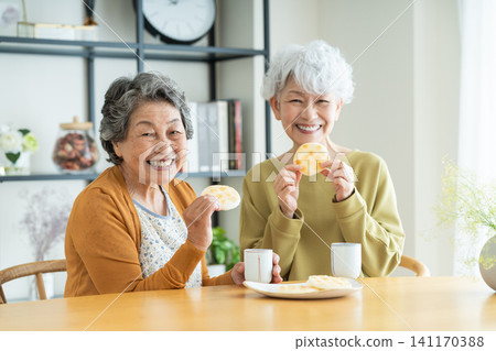 Senior woman eating rice crackers with a friend Senior woman eating rice crackers with a friend 141170388