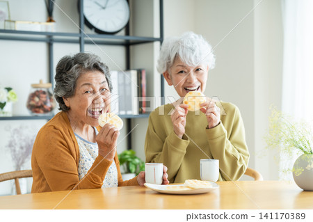 Senior woman eating rice crackers with a friend Senior woman eating rice crackers with a friend 141170389