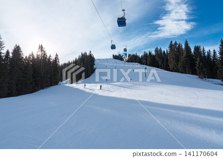 Skiers on a groomed slope with cable cars in the winter landscape of Saalbach in Austria Skiers on a groomed slope with cable cars in the winter landscape of Saalbach in Austria 141170604