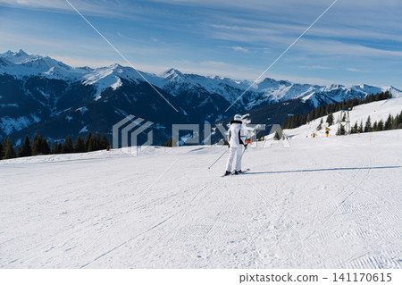 Skier standing on a groomed slope in Saalbach Austria with scenic snowy mountain peaks view Skier standing on a groomed slope in Saalbach Austria with scenic snowy mountain peaks view 141170615