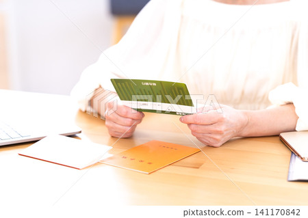 A senior woman's hands as she looks at her bankbook in the living room. A senior woman's hands as she looks at her bankbook in the living room. 141170842