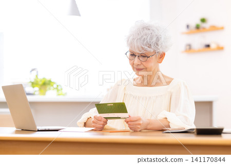 A senior woman looking at her bankbook in the living room A senior woman looking at her bankbook in the living room 141170844
