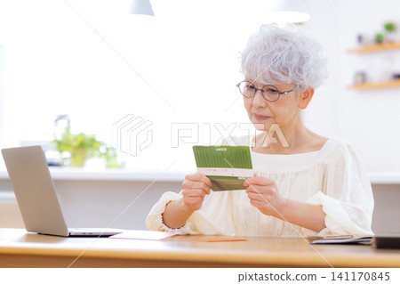 A senior woman looking at her bankbook in the living room A senior woman looking at her bankbook in the living room 141170845