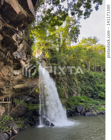 Waterfall flows from rocks into a calm river surrounded by trees 141171380