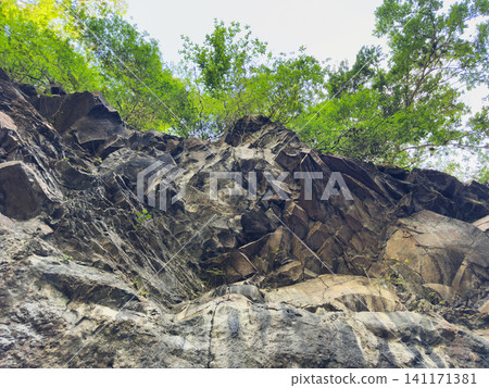 Rocky cliff under bright skies in a forested area 141171381