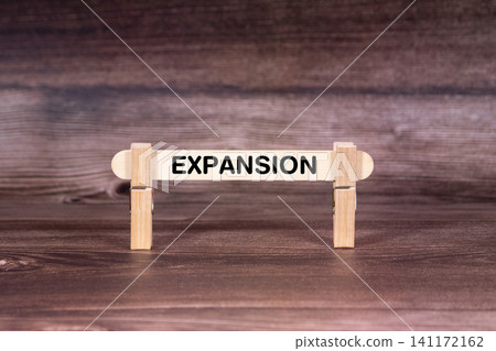 Expansion symbol. Clothespins gripping a wooden stick against a beautiful Brown Wooden Background . Business and Expansion concept with copy space Expansion symbol. Clothespins gripping a wooden stick against a beautiful Brown Wooden Background . Business and Expansion concept with copy space 141172162