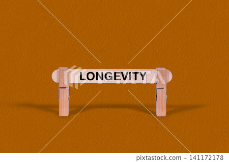 Longevity symbol. Wooden stick tightened by Clothespins, beautiful Orange color Backdrop. Business and Longevity concept with copy space Longevity symbol. Wooden stick tightened by Clothespins, beautiful Orange color Backdrop. Business and Longevity concept with copy space 141172178