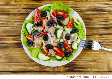 Tasty tuna salad with lettuce, black olives and fresh vegetables on wooden table. Top view Tasty tuna salad with lettuce, black olives and fresh vegetables on wooden table. Top view 141172276