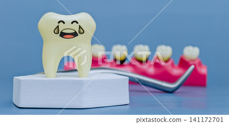 Sad crying tooth model on white podium with dental tool and jaw model with caries in blurred background. Pediatric dentistry concept. Sad crying tooth model on white podium with dental tool and jaw model with caries in blurred background. Pediatric dentistry concept. 141172701