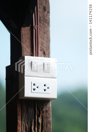 White electric wall outlet receptacle with switch and plug on wooden post use in Thailand 141174156