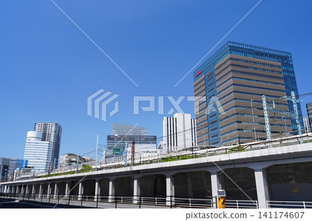 The cityscape of Yokohama's Minato Mirai district, with its towering skyscrapers and elevated railway tracks, stands out against a clear blue sky. 141174607