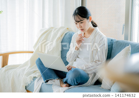 Woman using a laptop on the sofa Woman using a laptop on the sofa 141174632