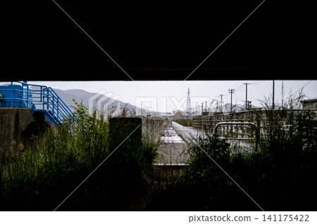 下雨天,透過低矮橋樑下令人壓抑的縫隙,可以看到水閘和混凝土堤岸。 下雨天,透過低矮橋樑下令人壓抑的縫隙,可以看到水閘和混凝土堤岸。 141175422