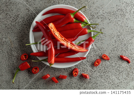 Fresh red chili peppers with green stems on a gray stone table. Fresh red chili peppers with green stems on a gray stone table. 141175435