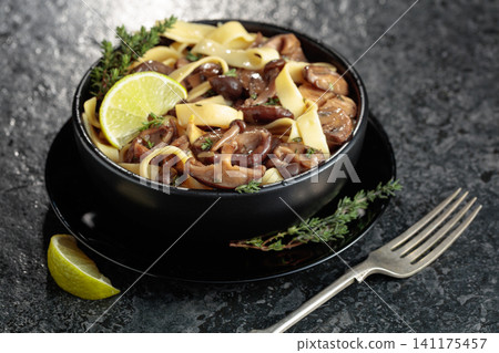 Shimeji and shiitake mushrooms stir-fried with soy sauce, garlic and thyme, served with noodles and lime slice in a black ceramic bowl. Shimeji and shiitake mushrooms stir-fried with soy sauce, garlic and thyme, served with noodles and lime slice in a black ceramic bowl. 141175457