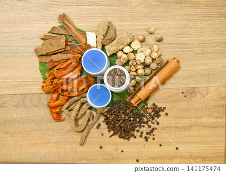 Top view of traditional Thai herbal ingredients for inhalers, including cloves, borneol, menthol, nutmeg, agarwood, black pepper, and camphor, arranged on a rustic wooden background, showcasing natura Top view of traditional Thai herbal ingredients for inhalers, including cloves, borneol, menthol, nutmeg, agarwood, black pepper, and camphor, arranged on a rustic wooden background, showcasing natura 141175474