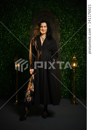 Woman stands in a dimly lit area with decorative plants and vintage lamps while holding a bag Woman stands in a dimly lit area with decorative plants and vintage lamps while holding a bag 141176021