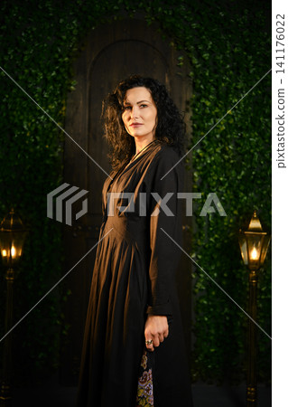 Woman stands confidently in black dress with green background and lights in evening setting Woman stands confidently in black dress with green background and lights in evening setting 141176022