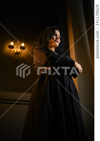 Woman stands in a dimly lit room with candles and natural light coming through a window Woman stands in a dimly lit room with candles and natural light coming through a window 141176029