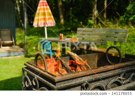 Fire pit burning wood in garden with seating area and wooden table Fire pit burning wood in garden with seating area and wooden table 141176055