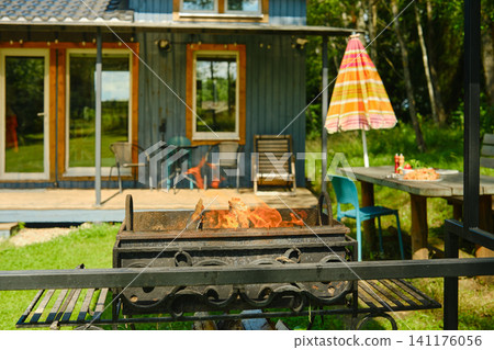 Grill on fire at outdoor gathering near wooden cabin in summer Grill on fire at outdoor gathering near wooden cabin in summer 141176056