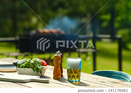 Barbecue gathering in garden with glass of beer and fresh vegetables on table Barbecue gathering in garden with glass of beer and fresh vegetables on table 141176062