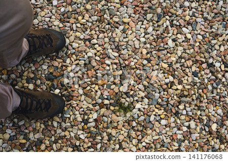 Person stands on gravel ground covered with small stones in outdoor area Person stands on gravel ground covered with small stones in outdoor area 141176068
