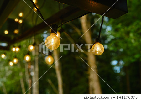String lights hang from roof in wooded area during evening time String lights hang from roof in wooded area during evening time 141176073